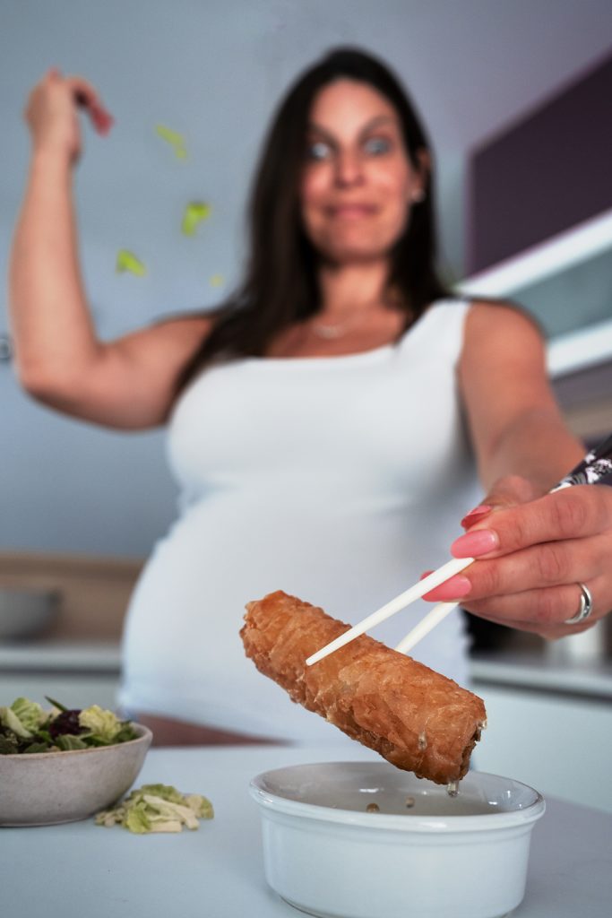 femme enceinte attrapant un nem avec des baguettes dans une cuisine