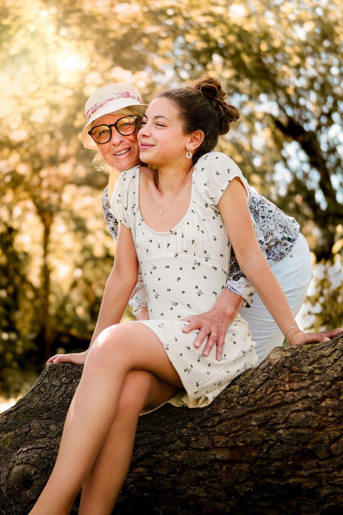 grand-mère et petite-fille complices assises sur un arbre pendant une séance photo famille en nature