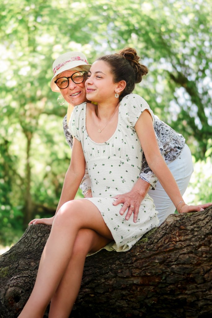 grand-mère et petite-fille complices assises sur un arbre pendant une séance photo famille en nature